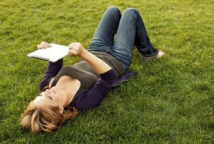 Girl lying in grass reading with a computer tablet